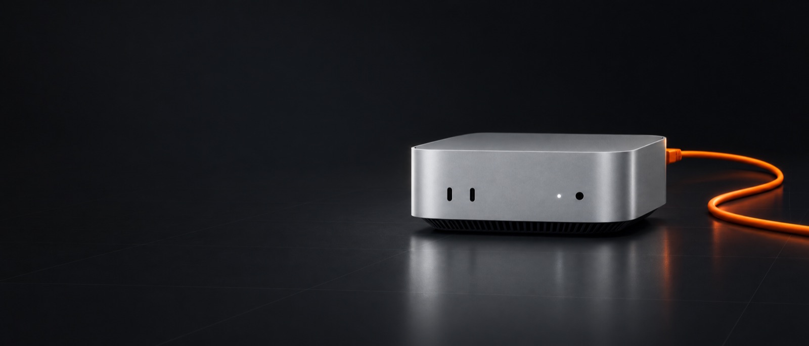 Der Mac mini auf dunklem Grund, ein orangefarbenes Netzwerkkabel führt nach hinten