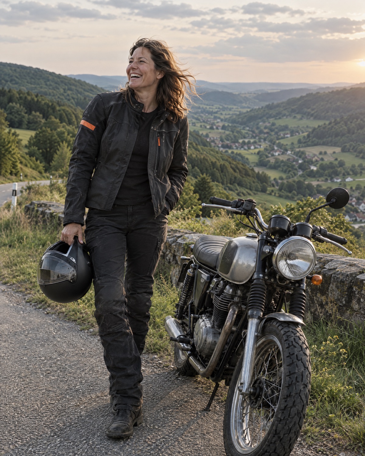 Eine Elektrikerin steht lachend neben ihrem Motorrad an einem Aussichtspunkt